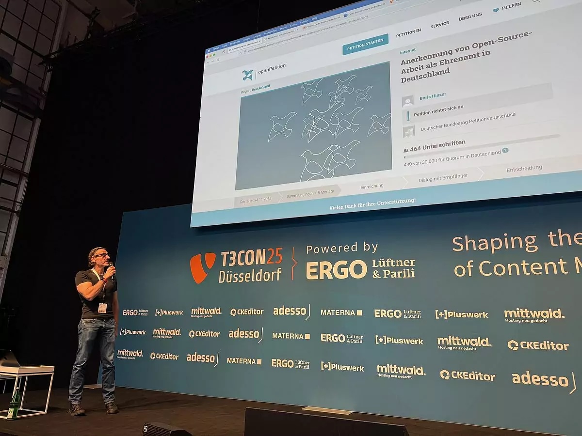 Boris zeigt auf der Bühne währen der T3CON die Peitiion zur Anerkennung von Open-Source als Ehrenamt, Bild: Wolfgang Wagner